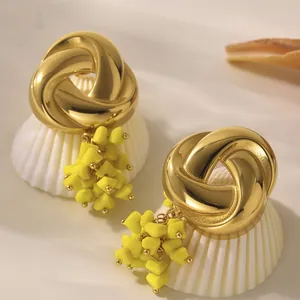 Goldene geometrische Ohrringe mit gelben Herzquasten auf einer weißen Muschel