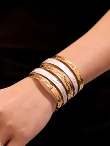 Dettaglio di bracciali multistrato placcati in oro 18k con smalto rosa sul polso