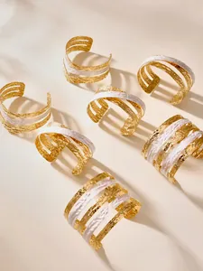 Dettaglio macro di bracciali a polsino multistrato placcati in oro 18k con smalto bianco