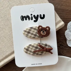 Détail de 2 barrettes à carreaux avec ours brodé et nœud en velours marron sur carte