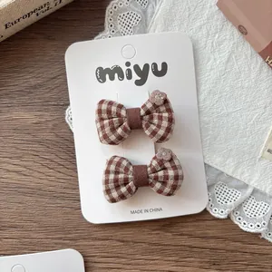 Detail view of plaid bow hair clips with embroidered flower on display card