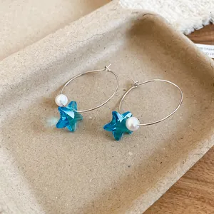 Primo piano di orecchini a cerchio in argento con stella di cristallo blu e perle.