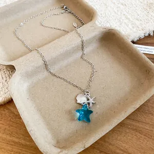 Dettaglio della collana con stella marina e conchiglia con ciondolo a stella blu su vassoio.