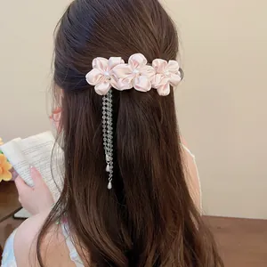 Close-up detail of pink fabric flower hair clip with pearl centers and dangling tassels.