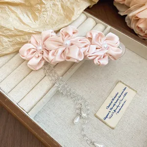 Close-up of elegant pink satin flower hair clip featuring pearls and beaded tassel details