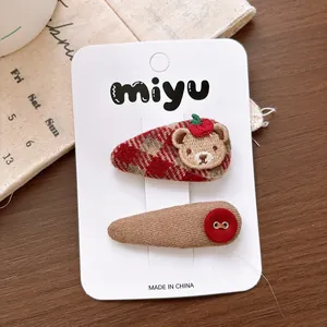 Detail of red plaid bow hair clip with bear embroidery and button on wooden table