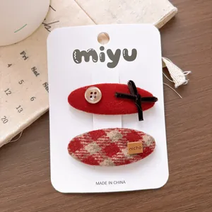 Detail of red bow hair clip and plaid BB clip set on white card over a wood background