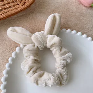 Detailed view of beige velvet scrunchie with rabbit ear bow on a white vintage tray