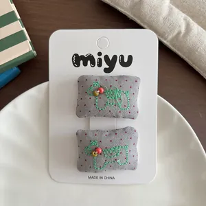 Dettaglio di fermagli in tessuto a pois grigi con ricamo animale verde su cartoncino