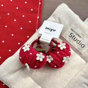 Detail of red knitted apple hair ties with white flower embroidery and pearl accents
