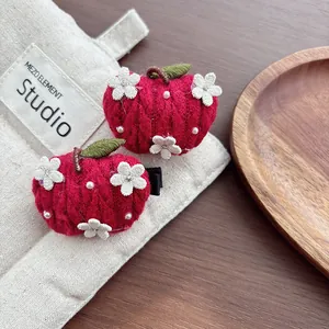 Close-up of handmade red knitted apple hair clips with white flowers and green leaves