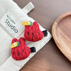 Close-up of red crochet rabbit hair clips with carrot and pearl details on linen