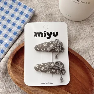 Detail of dark grey floral fabric hair clips with lace trim and tassel on a white card
