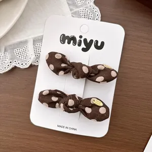 Détail de barrettes à nœuds à pois marron café avec petite étiquette métallique dorée