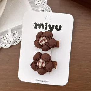 Détail de barrettes à fleurs en tissu marron avec centre à carreaux sur carte blanche