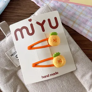 Close-up of cute orange pineapple hair clips set on a branded card for girls