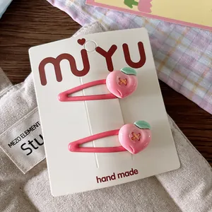 Detailed macro view of two pink handmade peach hair clips on a white display card