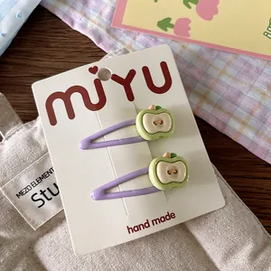 Detail view of two purple apple-shaped hair clips for girls on handmade display card