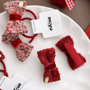Red tweed bow hair clips and elastic ties set with gold pendants on a ceramic plate