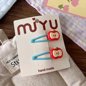 Detail of light blue metal hair clips with red apple charm on white display card