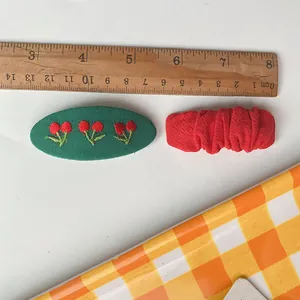 Detail van geborduurde groene kersenspeld en rode geplooide haarspeld met liniaalmaat
