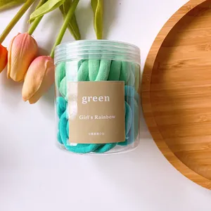 Gros plan d'élastiques à cheveux vert dégradé dans un pot cylindrique transparent