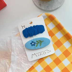 Detail van geborduurde bloemen haarspeld en marineblauwe geplooide stoffen clip set