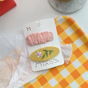 Detail van roze gerimpelde stof en geborduurde ovale haarklemmetjes op displaykaart
