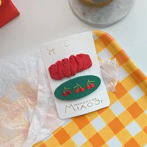 Detail van geborduurde kersenvormige haarspeldjes op presentatiekaart voor meisjes