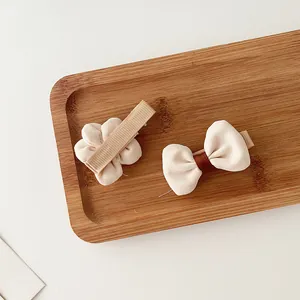 Floral and bow-knot fabric hair clips in beige, set for girls on a natural wooden tray