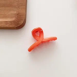Détail d'une petite pince à cheveux orange vif avec un design incurvé croisé élégant