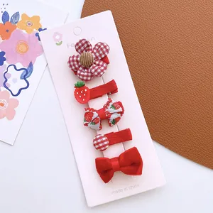 Close-up of 5 red girls' hair clips with strawberry and floral fabric patterns