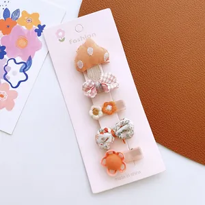 Close-up of four assorted floral and bow fabric hair clips on a pink display card
