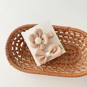 Close-up of beige fabric flower and bow hair clips in a small woven basket for girls