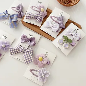 Detalle de pinzas para el cabello con lazo morado y flores de tela en tarjeta blanca