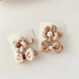 Detail of beige fabric flower and bow hair clips for girls on a white card display