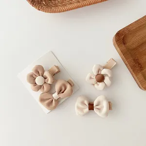 Set of four floral and bow fabric hair clips in soft cream and beige tones on display card