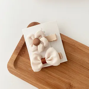Detail of fabric flower and bow hair clip set in beige on a wooden display tray