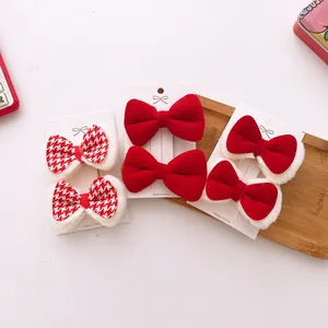 Close-up of red velvet and houndstooth bow hair clips with white plush trim on display card