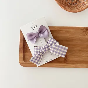 Primer plano de pinzas para el cabello con lazo de satén morado y cuadros en tarjeta