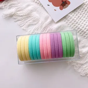 Close-up of pastel elastic hair ties in a transparent box on a white fabric background