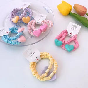 Set de chouchous à pendentif cœur pastel lavande et rose présentés avec tulipes