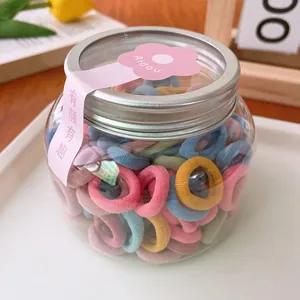 Close-up of colorful mini elastic hair ties in a clear plastic jar with floral label