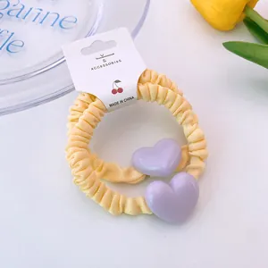 Détail de deux chouchous plissés jaunes avec breloques cœur violet sur carte de présentation