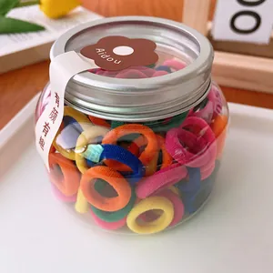 Macro shot of candy-colored elastic hair ties inside a clear jar with silver screw lid