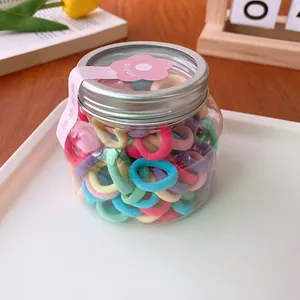 Colorful candy-colored mini hair elastics set in a transparent storage jar on a white tray