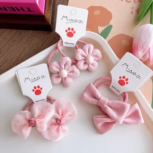 Set of three pink fabric flower and bow hair ties for girls on a white display tray