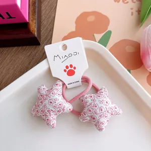 Detail showing two floral star-shaped elastic hair ties in sweet pink cotton fabric