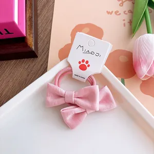 Detailed view of light pink fabric bow hair tie for girls on a white decorative plate