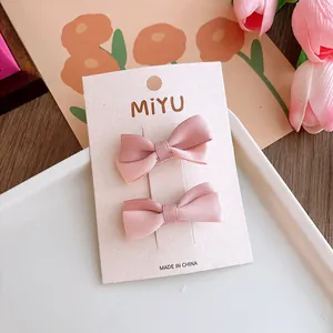 Dettaglio di due fermagli per capelli con fiocco in raso rosa su carta di marca